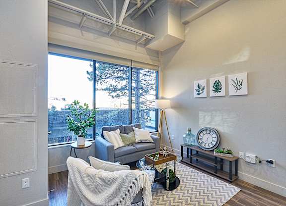 A living room with a grey couch, a white chair, and a wooden coffee table at Brickside Heights Apartments, Utah