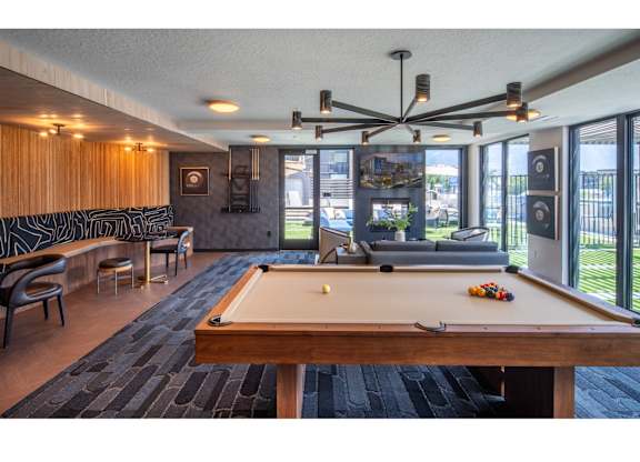 A pool table is in the middle of a room with a view of the outside.