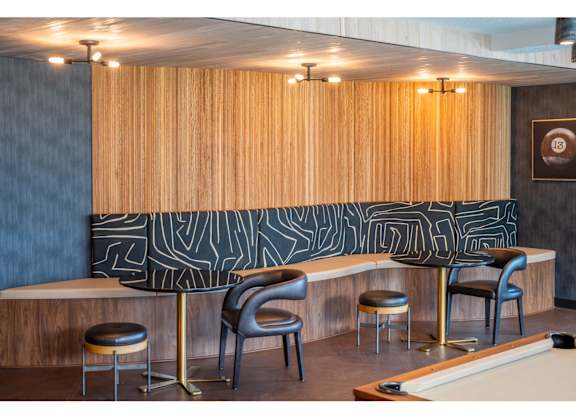 A pool table is in the middle of a room with a wood panelled wall and a black and white patterned wallpaper.
