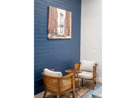 A painting of a building is hanging on a blue wall above a chair and a table.