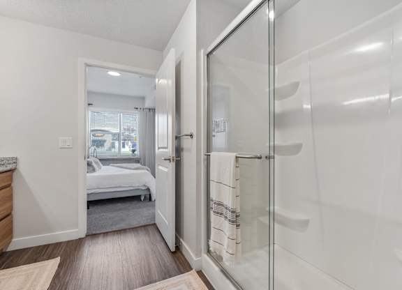 a white bathroom with a glass shower and a bedroom at The Flats at Riverwoods, Provo, Utah
