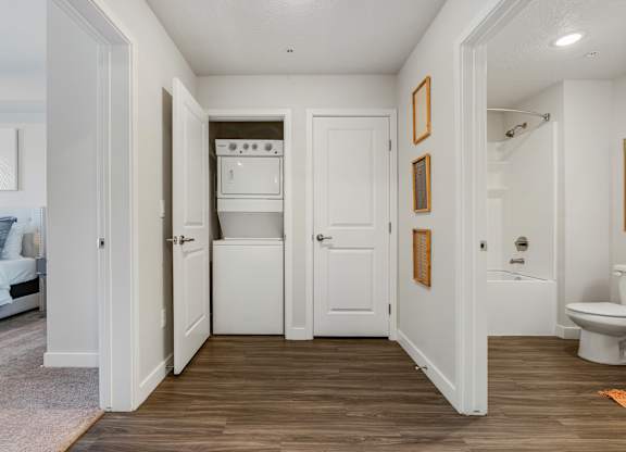 a hallway with a toilet and a washer and dryer in a white room at The Flats at Riverwoods, Provo, UT, 84604