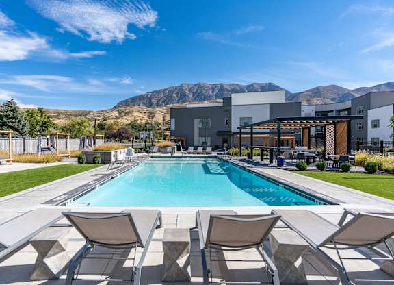 a swimming pool with chairs and a building in the background at The Flats at Riverwoods, Provo, UT, 84604
