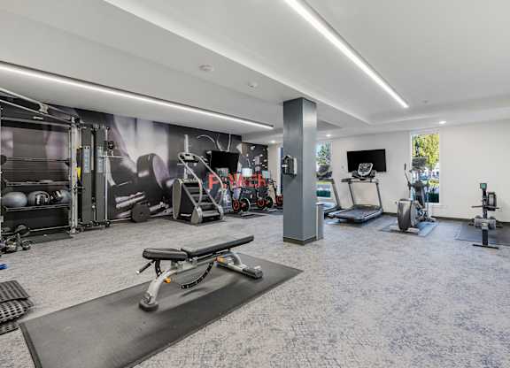 a gym with weights and cardio equipment in a room with a mural on the wall at The Flats at Riverwoods, Provo, Utah