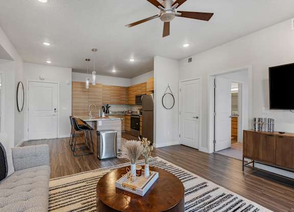 a living room with a couch and a table in front of a kitchen at The Flats at Riverwoods, Provo