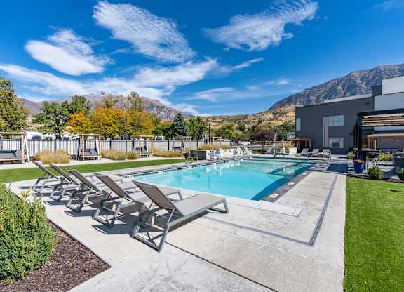 a swimming pool with patio furniture and a building with mountains in the background at The Flats at Riverwoods, Provo, UT