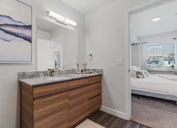 a bathroom with a vanity and a mirror and a bedroom with a bed at The Flats at Riverwoods, Provo, 84604