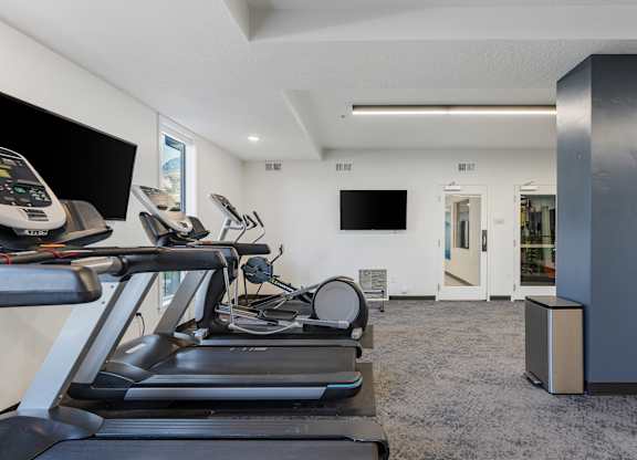 the gym has cardio equipment and a flat screen tv at The Flats at Riverwoods, Provo, UT, 84604