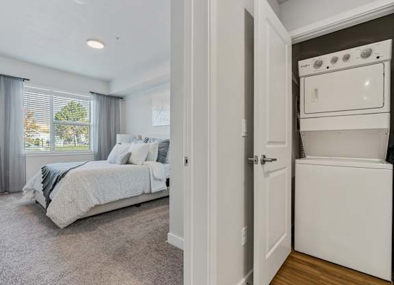 a bedroom with a bed and a washer and dryer next to a closet at The Flats at Riverwoods, Provo, Utah