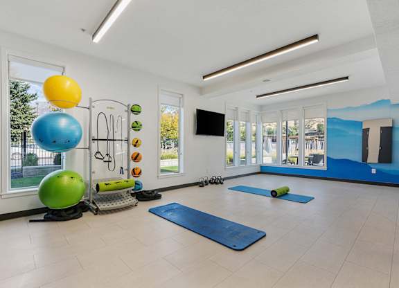 a workout room with yoga mats and a colorful ball and a large window at The Flats at Riverwoods, Provo, UT