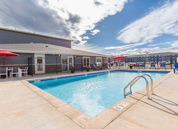 A pool with a red umbrella and a building in the background. at Red Rock Apartments, Rapid City, 57702