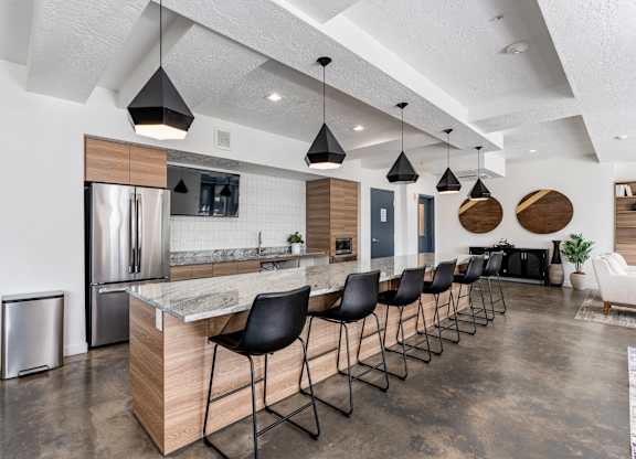 a kitchen with a long island with black chairs and a stainless steel refrigerator at The Flats at Riverwoods, Provo