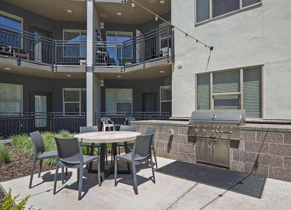 a patio with a table and chairs and a grill at The Flats at Riverwoods, Provo, Utah