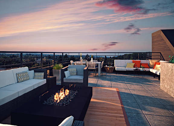 A patio with a fire pit and seating area overlooking a cityscape at dusk.