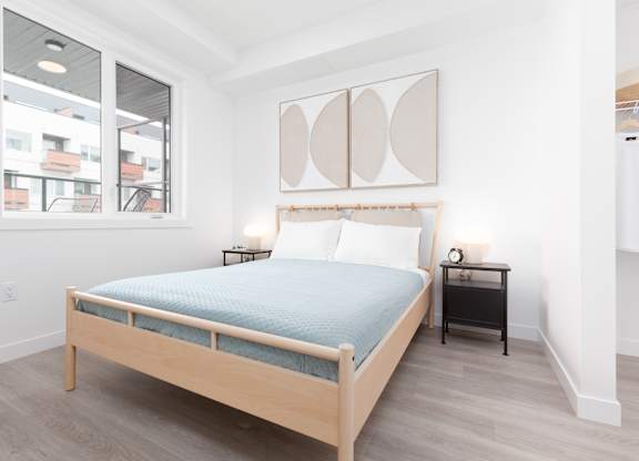 A bedroom with a bed, nightstand, and a painting on the wall.