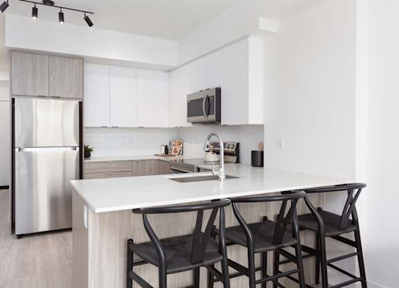 A modern kitchen with a white countertop and black chairs.