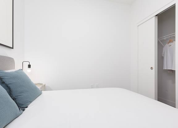 A white bed with a blue pillow and a white wall.