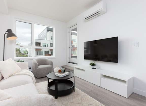 A modern living room with a white sofa, a black coffee table, and a flat-screen TV mounted on the wall.