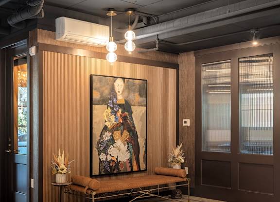 A large painting hangs on a wall above a bench in a room with a ceiling light fixture.