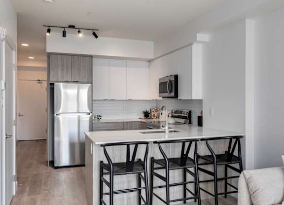 A modern kitchen with a white island and black barstools.