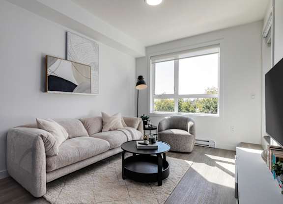 A living room with a grey couch, a black coffee table, and a large window.