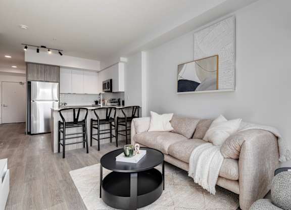 A modern living room with a grey couch, a coffee table, and a dining area in the background.