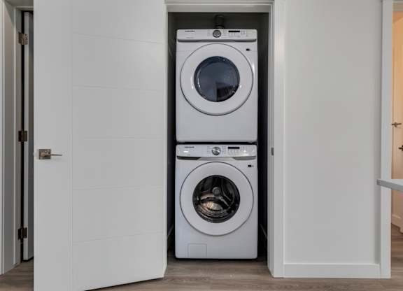 A white washing machine is in a small white laundry room.