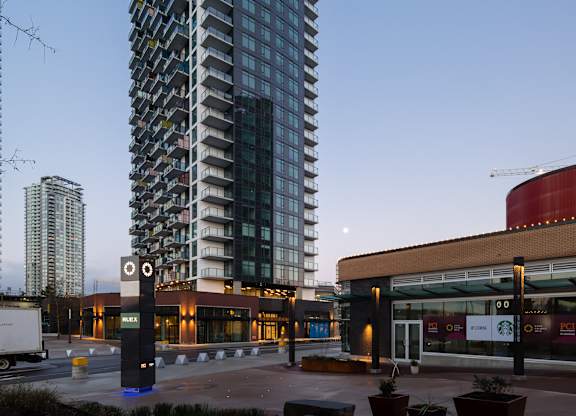 A tall building with many windows is lit up at dusk.