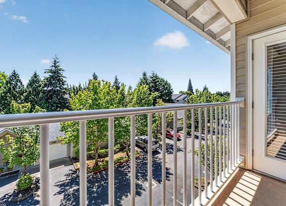 A balcony with a white railing overlooks a street with cars and houses.