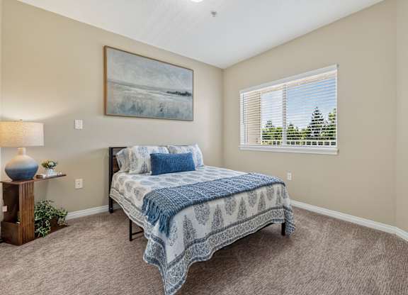 A bedroom with a bed, lamp, and painting on the wall.