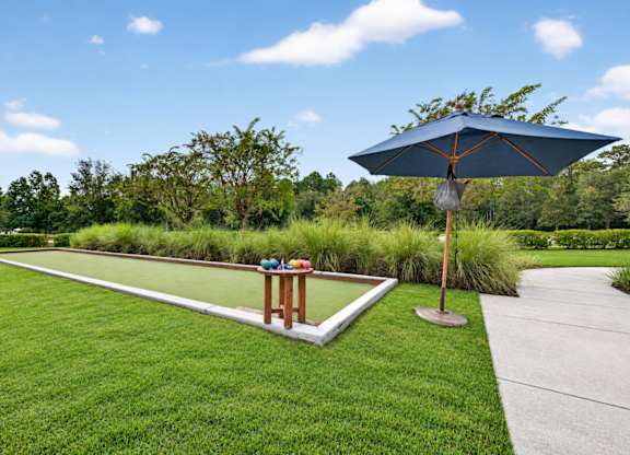 A blue umbrella stands on a concrete slab in a grassy area.
