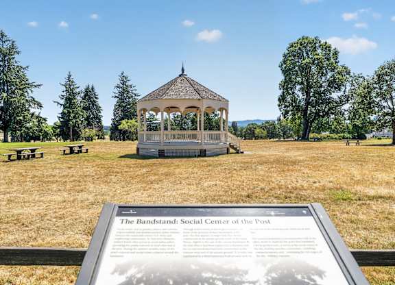 A gazebo is in the middle of a field with a sign in front of it.