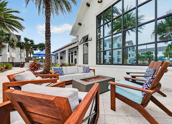 A patio with wooden chairs and a table with a white cushion.