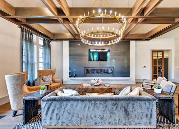 Clubhouse with lounge seating, arm chairs and a couch with a large chandelier and fire place and large tv above the fireplace, wood and stone accents throughout the room