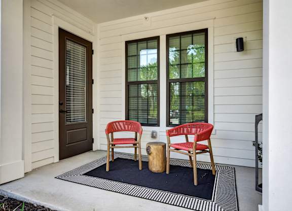 Two red chairs are placed on a black and white striped rug on a  patio