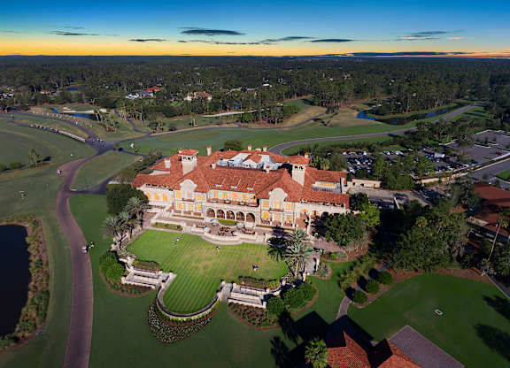 A large, beautifully designed building with a red roof is surrounded by a well-kept lawn and a winding path.