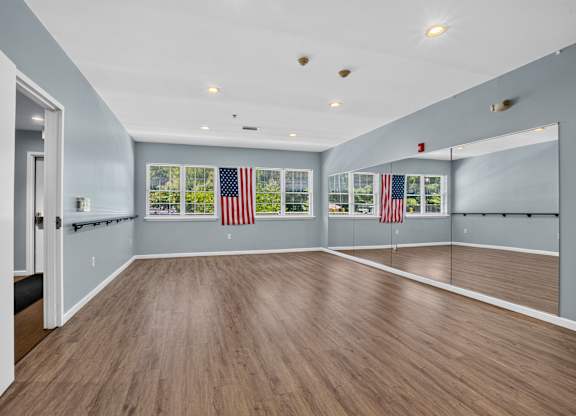 A spacious room with wooden flooring and American flags on the windows.
