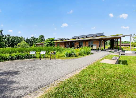 A building with a green roof is surrounded by greenery and has a paved walkway leading to it.