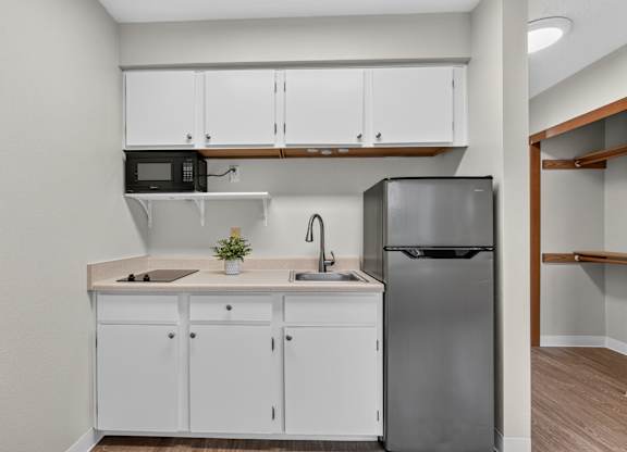 A kitchen with white cabinets and a black fridge. Kitchenette style with beige walls