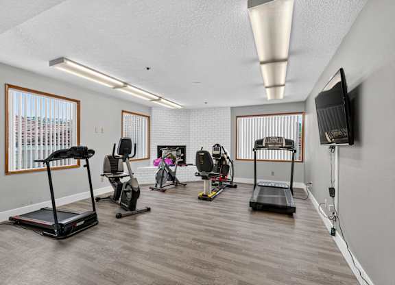 Fitness center with a treadmill, exercise bike, and other equipment. Also a tv mounted on the wall.