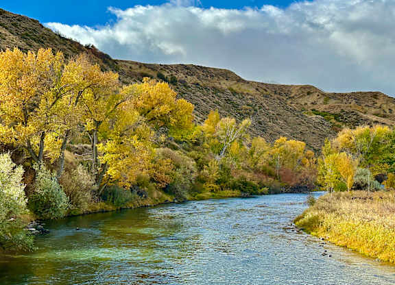 A river flows through a valley with trees showing autumn colors.