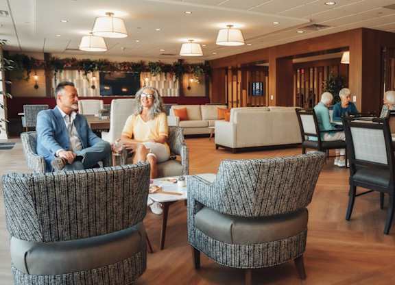 A group of people are sitting in a waiting area with comfortable chairs and a reception desk.