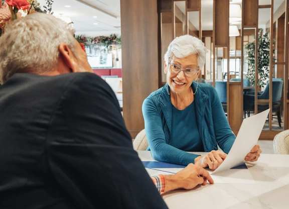 A man and a woman are sitting at a table, with the woman holding a piece of paper.
