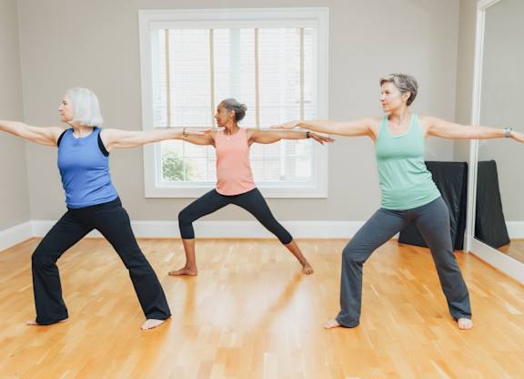 Three women are practicing yoga in a room with wooden floors.