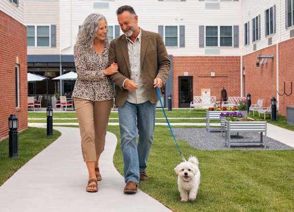 A man and woman walking a dog on a leash.