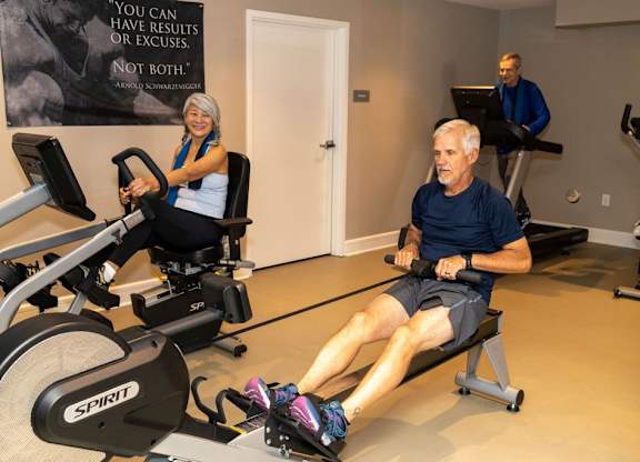 A man and a woman are exercising on rowing machines in a gym.