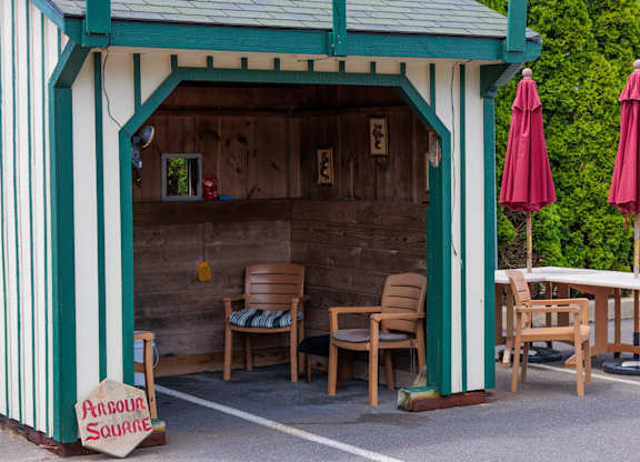 A small wooden building with a green trim and a sign that says "Around Square".