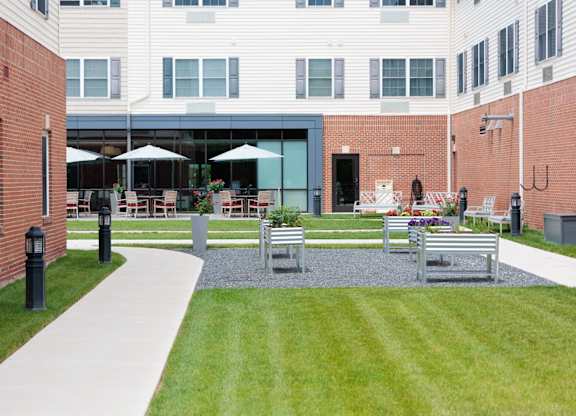 A courtyard with a white pathway, a grassy area, and a building in the background.