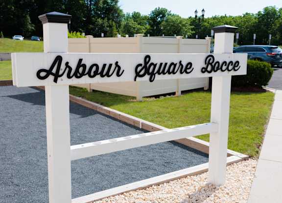 A white sign with black lettering that says Arbour Square Bocce.