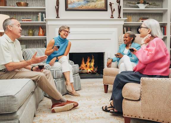 A group of people are sitting in a living room by a fireplace.